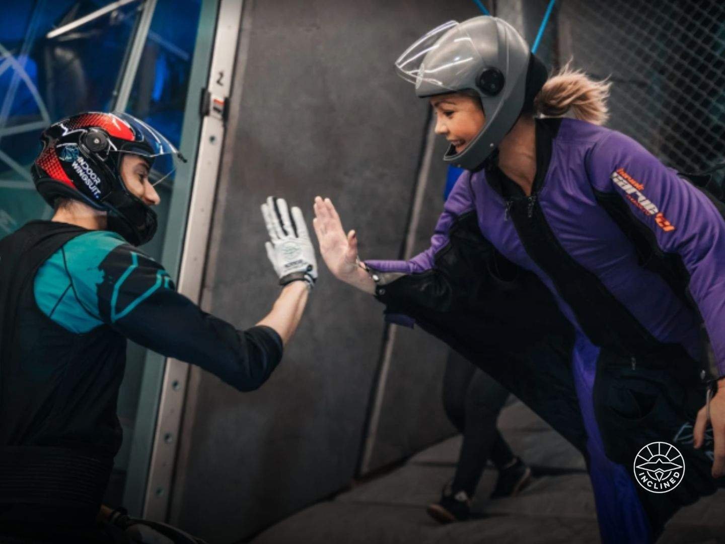 First-time flyer in an indoor wingsuit tunnel, guided by an instructor, experiencing controlled human flight for the first time.